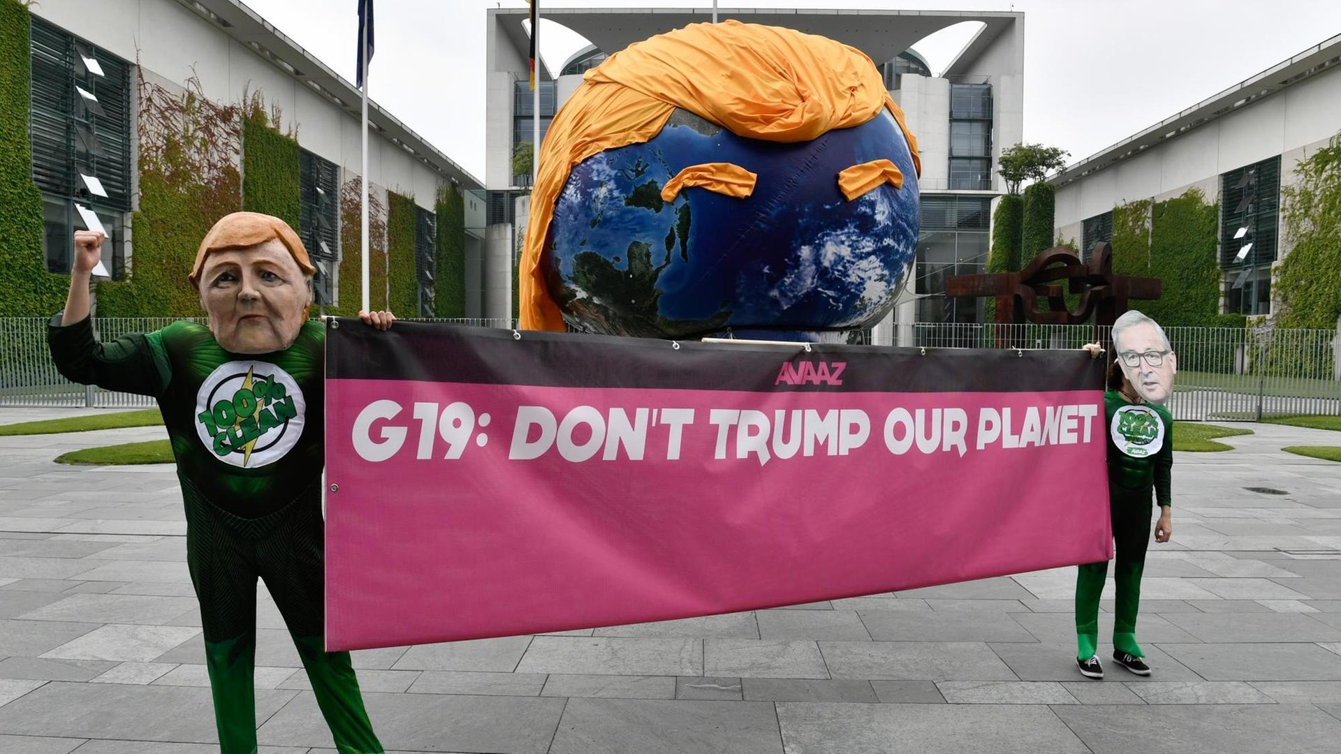 Aktivisten mit Masken von Bundeskanzlerin Merkel und EU-Kommissionspräsident Juncker halten vor dem Kanzleramt in Berlin ein Banner mit der Aufschrift: "G19: Don't trump our planet". Aktivisten mit Masken von Bundeskanzlerin Merkel und EU-Kommissionspräsident Juncker halten vor dem Kanzleramt in Berlin ein Banner mit der Aufschrift: "G19: Don't trump our planet".