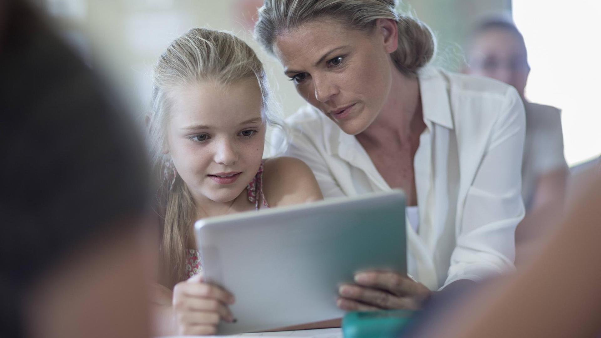 Schülerinnen und ihre Lehrerin beugen sich über ein Tablet Schülerinnen und ihre Lehrerin beugen sich über ein Tablet