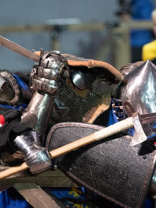 Zwei Kämpfer in mittelalterlicher Rüstung, mit Schild, Helm und Schwert.