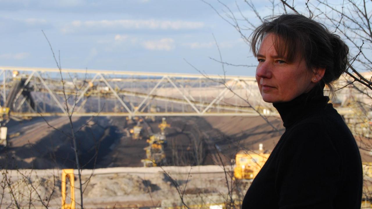 Sybille Tetsch steht am Rande des Waldes, im Hintergrund der Braunkohletagebau bei Proschim mit Vorschnittbaggern und Förderbrücke F60. Sybille Tetsch steht am Rande des Waldes, im Hintergrund der Braunkohletagebau bei Proschim mit Vorschnittbaggern und Förderbrücke F60.
