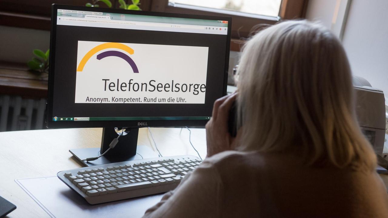 Eine ehrenamtliche Mitarbeiterin der evangelischen Telefonseelsorge München hält einen Telefonhörer an einem Arbeitsplatz für Seelsorger während die Homepage der Telefonseelsorge auf einem Monitor zu sehen ist. Eine ehrenamtliche Mitarbeiterin der evangelischen Telefonseelsorge München hält einen Telefonhörer an einem Arbeitsplatz für Seelsorger während die Homepage der Telefonseelsorge auf einem Monitor zu sehen ist.