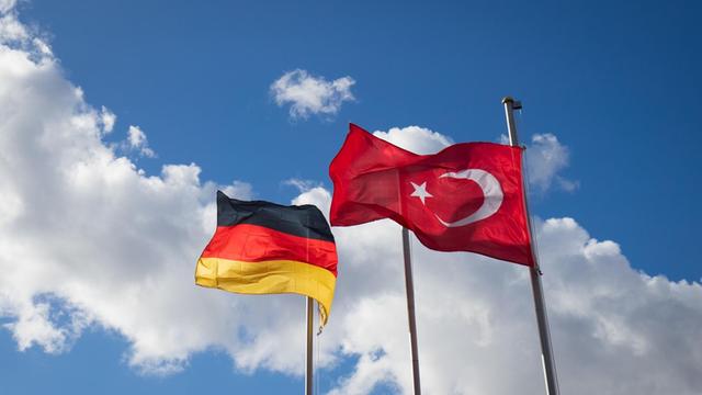 Die deutsche und die türkische Flagge sind an Fahnenmasten zu sehen. Im Hintergrund ziehen Wolken auf.