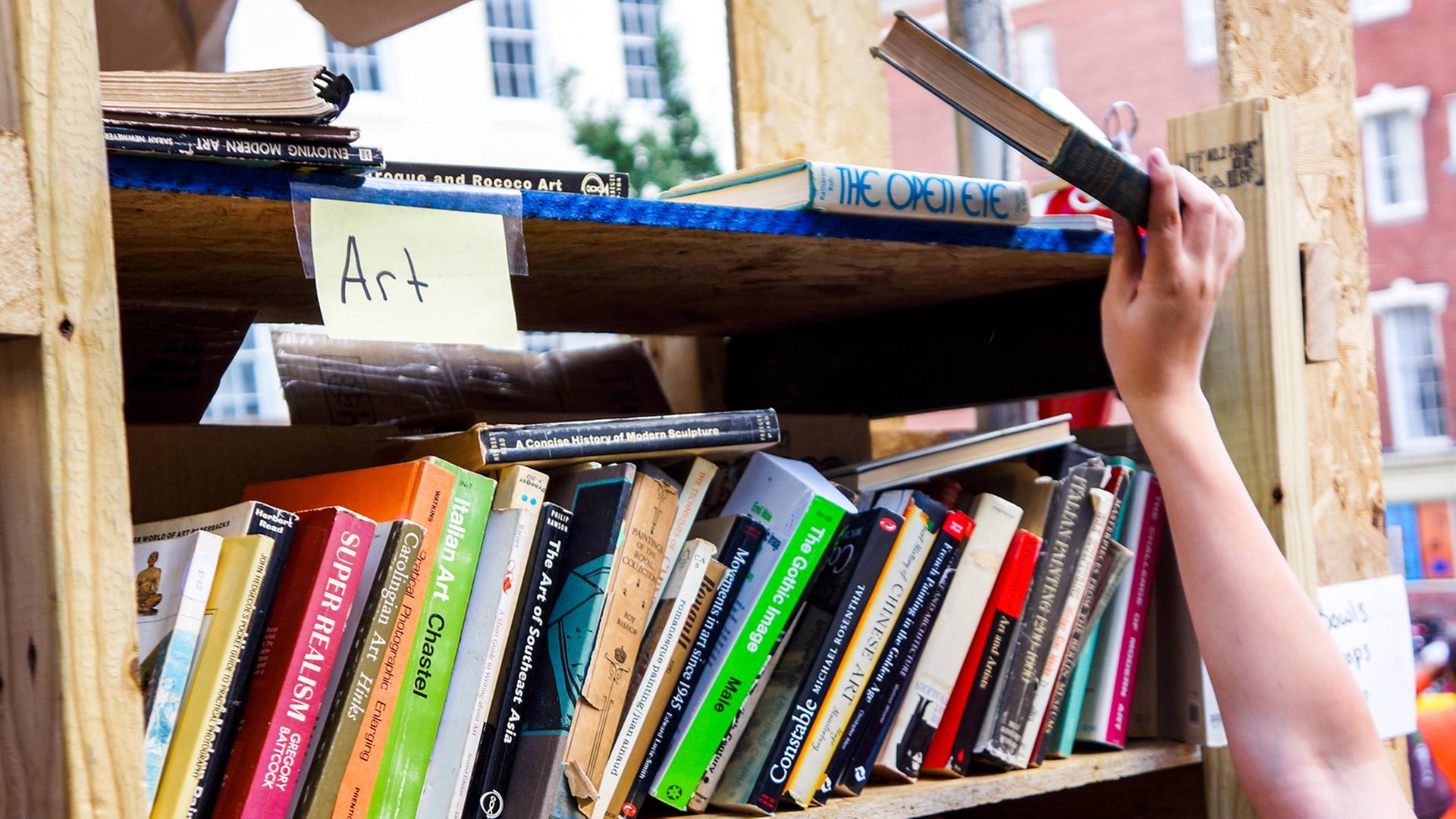 Eine Hand greift ein Buch aus einem Regal mit gebrauchten Büchern.