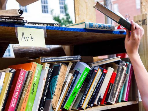 Eine Hand greift ein Buch aus einem Regal mit gebrauchten Büchern.