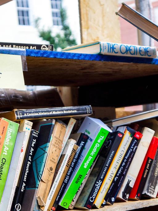 Eine Hand greift ein Buch aus einem Regal mit gebrauchten Büchern.