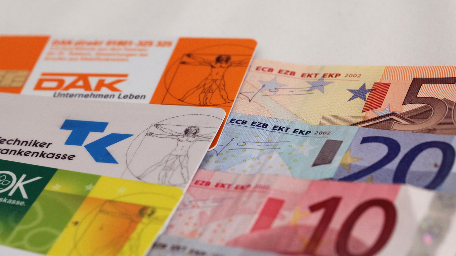 Neben Versichertenkarten verschiedener Krankenkassen liegen mehrere Geldscheine. Neben Versichertenkarten verschiedener Krankenkassen liegen mehrere Geldscheine.