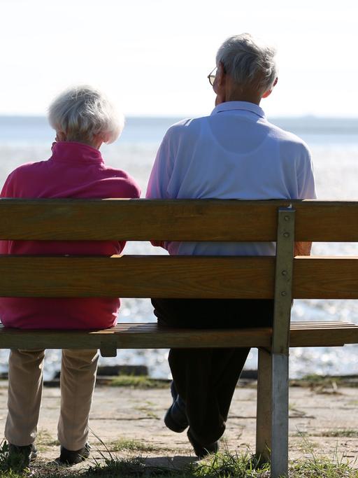 Ein Senioren-Paar sitzt auf einer Bank und schaut auf das im Watt.