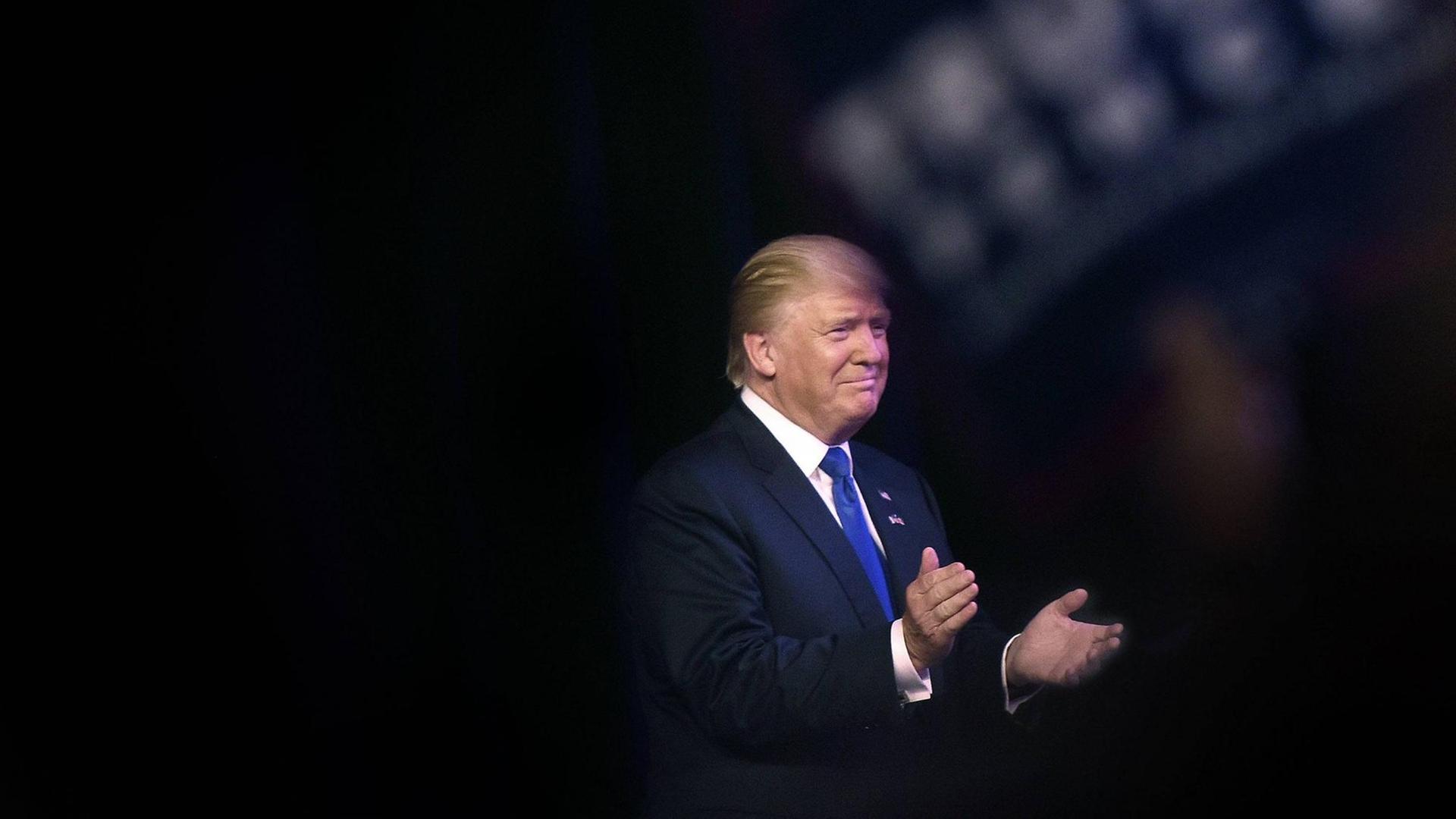 Sie sehen Donald Trump auf einer Bühne, er klatscht in die Hände. Sie sehen Donald Trump auf einer Bühne, er klatscht in die Hände.