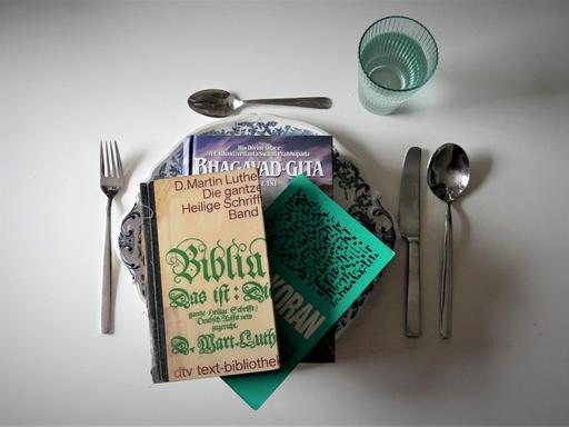 Auf einem Tisch ist ein Essgedeck angerichtet - Serviert werden religiöse Schriften