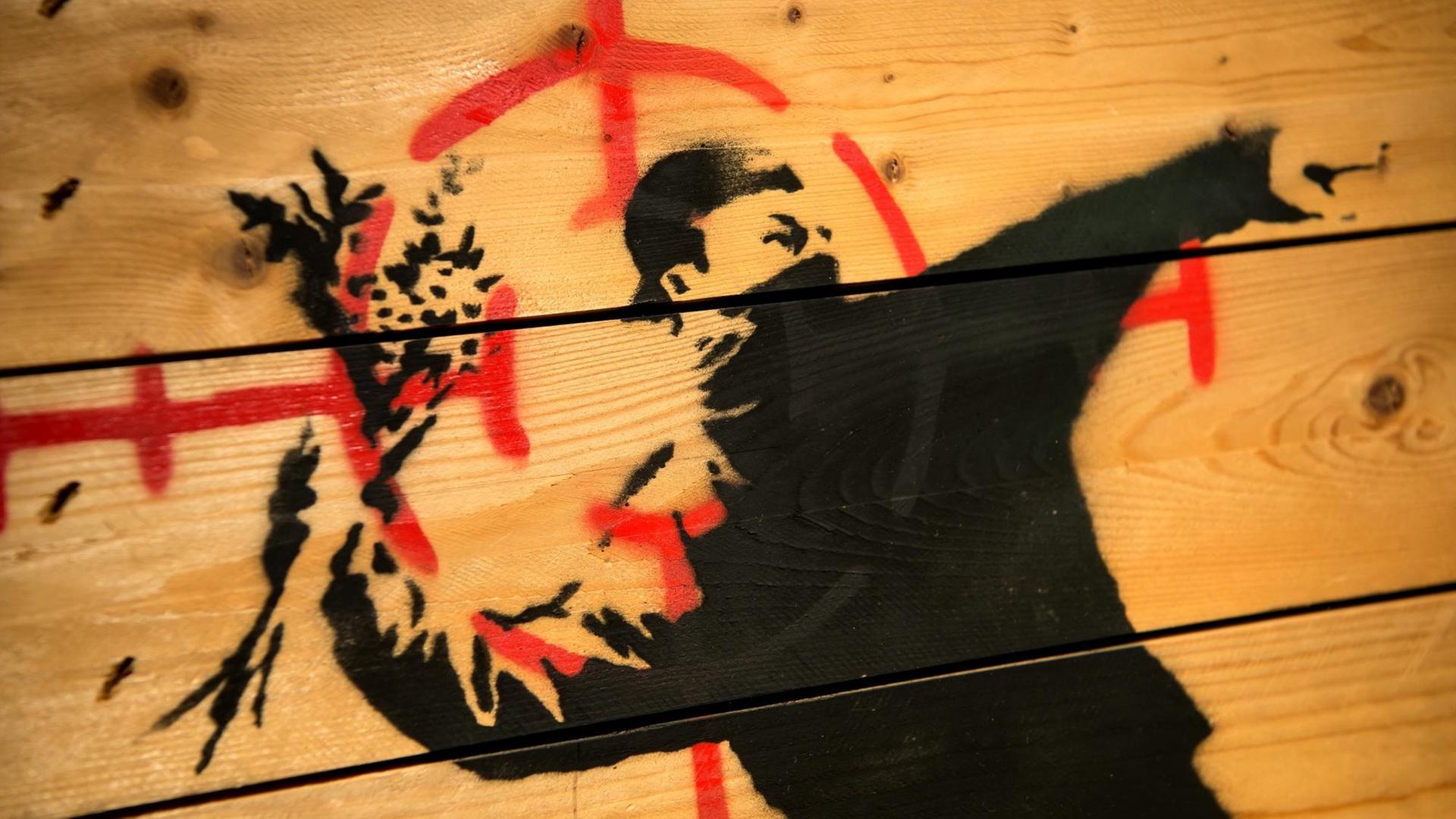 Graffii von Banksy zeigt einen Vermummten, der ausholt um einen Strauß Blumen zu werfen.