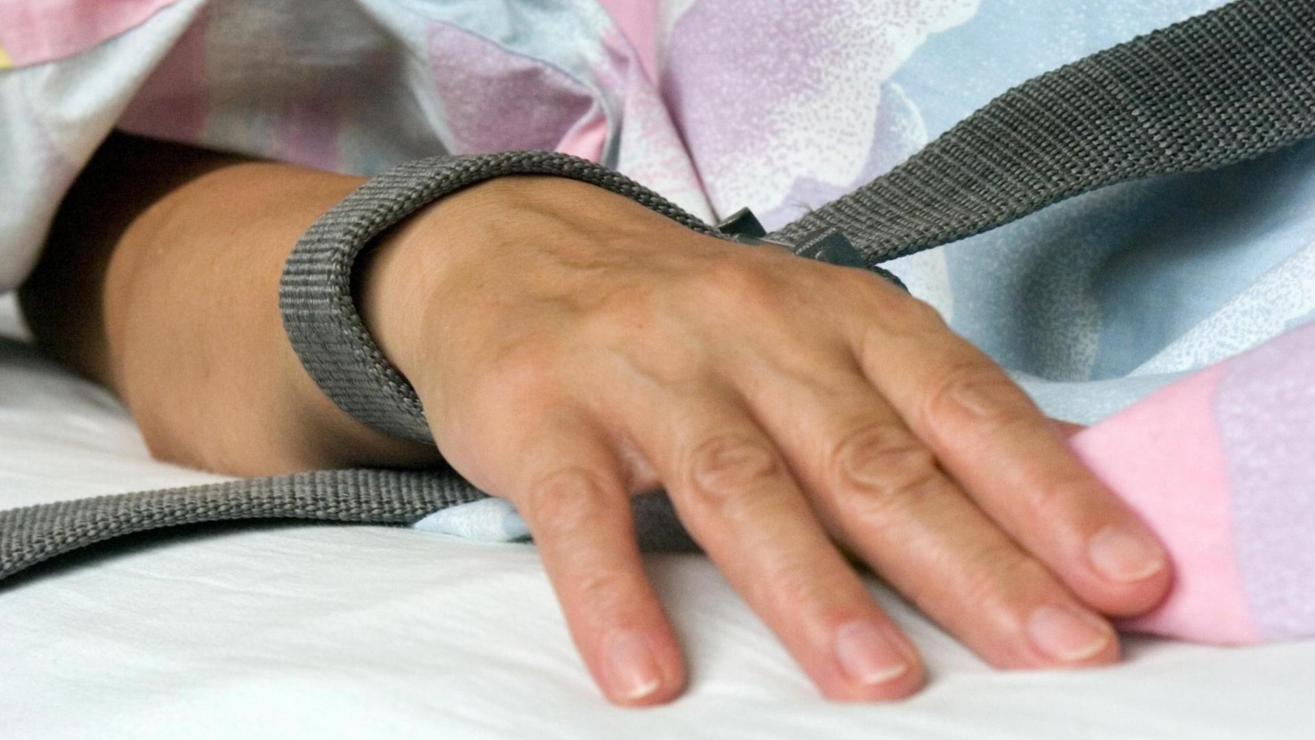 Das Foto zeigt eine mit einem Textilband festgebundene Hand eines Patienten. Das Foto zeigt eine mit einem Textilband festgebundene Hand eines Patienten.