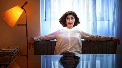 Nava Ebrahimi sitzt auf einem Sofa und guckt in die Kamera. Ihre Arme liegen auf der Lehne.