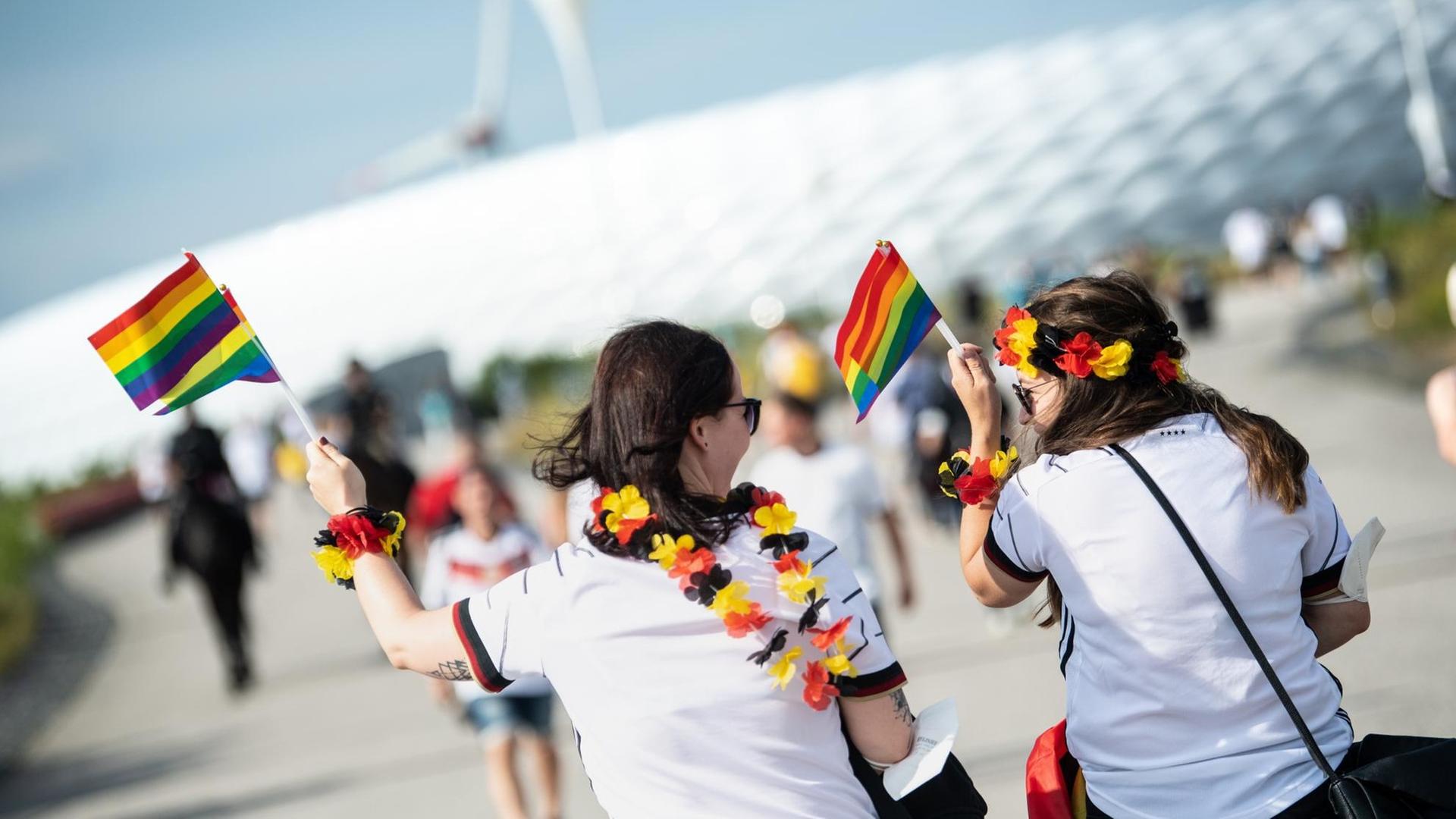 Zwei weibliche Fußballfans kommen mit Regenbogenfahnen zum Stadion in München. Zwei weibliche Fußballfans kommen mit Regenbogenfahnen zum Stadion in München.
