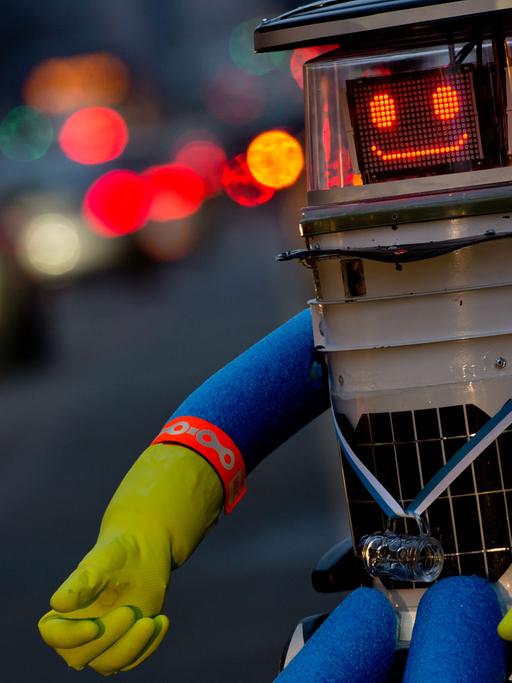 Der trampende Roboter hitchBOT sitzt am 12.02.2015 in München am Straßenrand und lächelt in die Kamera.