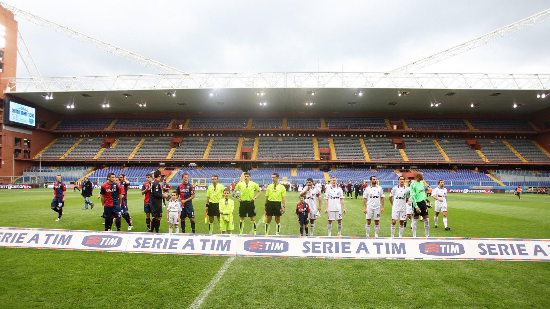 Zu sehen sind die Mannschaften von Genua und Mailand auf dem Rasen, im Hintergrund leere Tribünen.