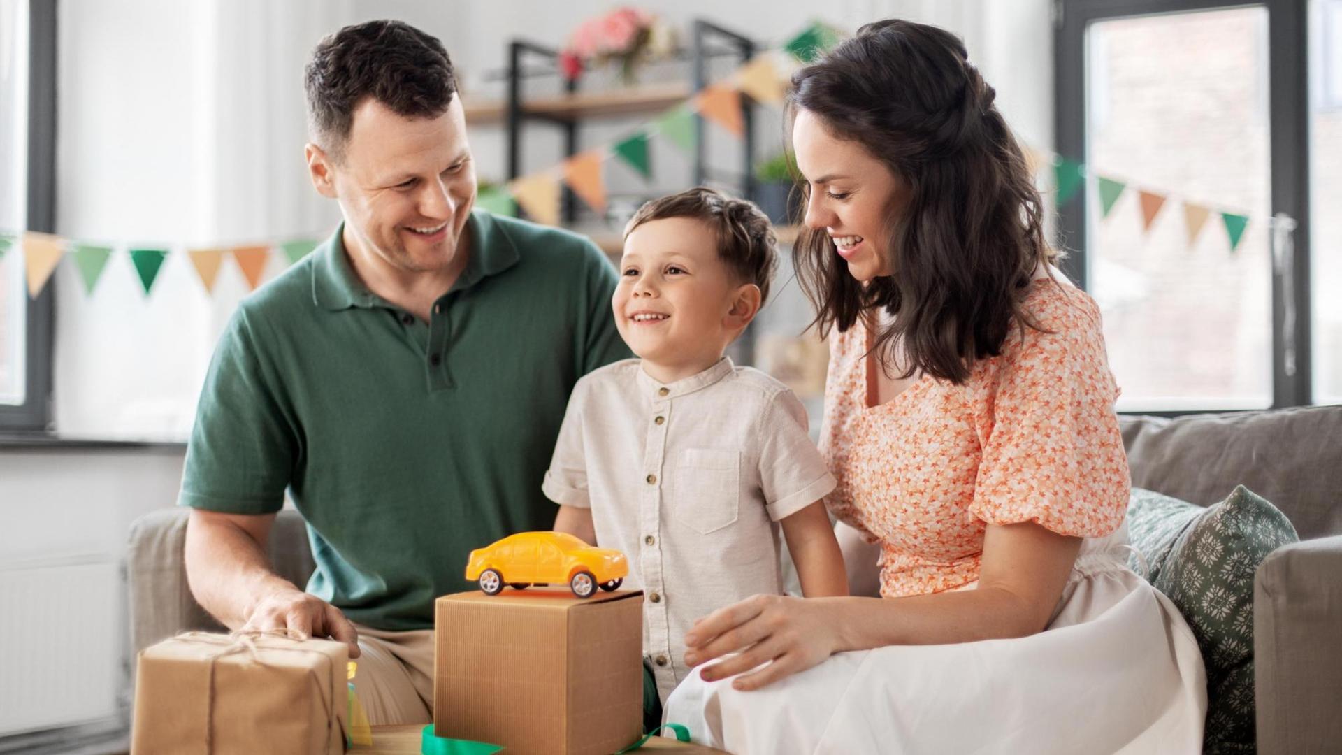 Eine Mutter und ein Vater sitzen links und rechts von ihrem Sohn, der sich über ein Geschenk freut. Eine Mutter und ein Vater sitzen links und rechts von ihrem Sohn, der sich über ein Geschenk freut.