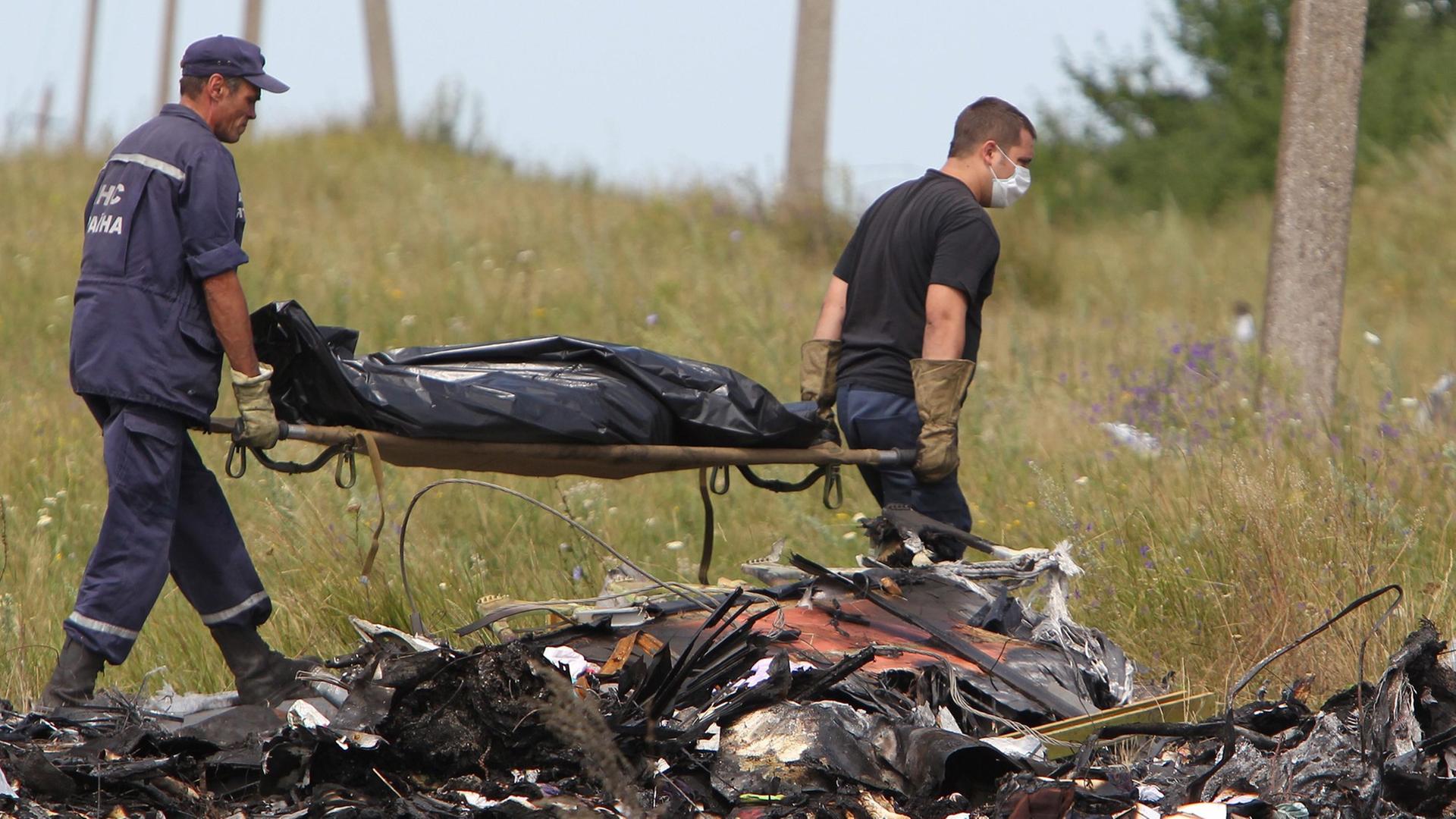 Hinter Trümmern tragen zwei ukrainische Arbeiter eine Bahre, auf der ein abgedecktes Todesopfer liegt. Hinter Trümmern tragen zwei ukrainische Arbeiter eine Bahre, auf der ein abgedecktes Todesopfer liegt.