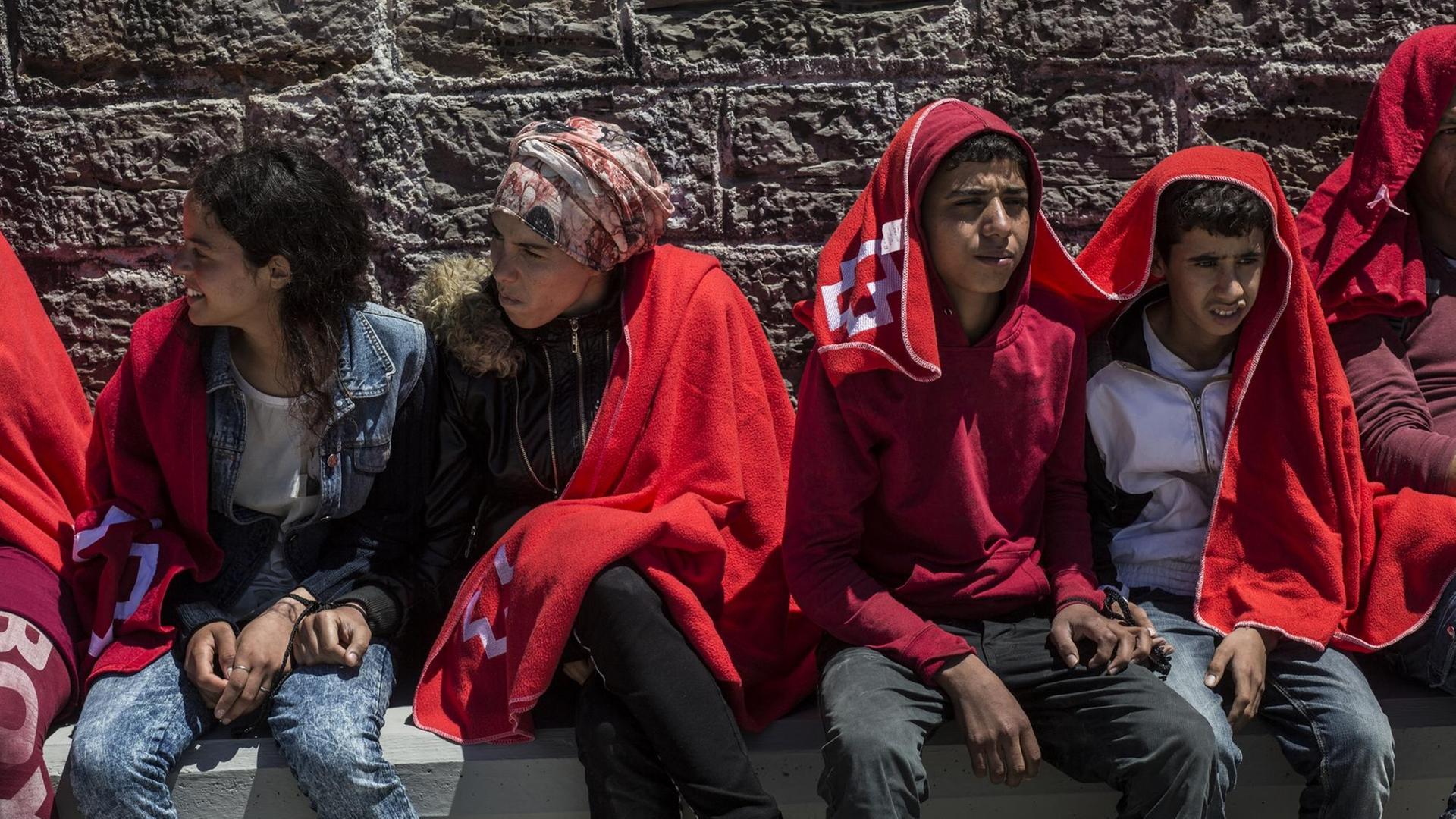 29.06.2018, Spanien, Tarifa: Junge Migranten aus Nordafrika sitzen nach ihrer Rettung in der Straße von Gibraltar im Hafen von Tarifa in Decken gehüllt an einer Mauer. Ihre Hände wurden zuvor zusammengebunden. Die EU-Staaten haben sich bei ihrem Gipfel in Brüssel darauf geeinigt, in der EU geschlossene Aufnahmelager für gerettete Bootsflüchtlinge einzurichten. Foto: Javier Fergo/dpa | Verwendung weltweit 29.06.2018, Spanien, Tarifa: Junge Migranten aus Nordafrika sitzen nach ihrer Rettung in der Straße von Gibraltar im Hafen von Tarifa in Decken gehüllt an einer Mauer. Ihre Hände wurden zuvor zusammengebunden. Die EU-Staaten haben sich bei ihrem Gipfel in Brüssel darauf geeinigt, in der EU geschlossene Aufnahmelager für gerettete Bootsflüchtlinge einzurichten. Foto: Javier Fergo/dpa | Verwendung weltweit