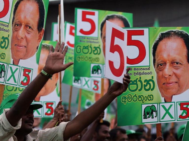 Menschen in Sri Lanka halten Wahlplakate mit dem Konterfei von Maithripala Sirisena in die Höhe.