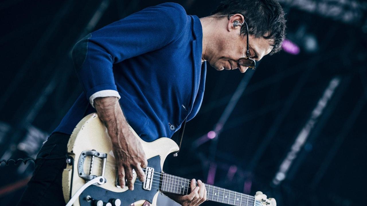 Ein Mann im blauen Sakko mit Gitarre steht auf ener Bühne. Ein Mann im blauen Sakko mit Gitarre steht auf ener Bühne.
