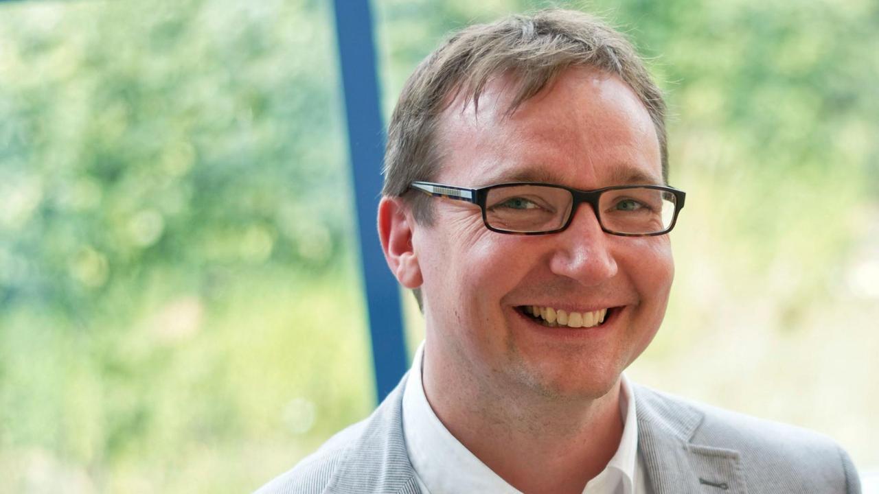Oliver Wille lächelt in die Kamera vor einem großen Fenster stehend, dass den Blick ins Grüne gewährt. Oliver Wille lächelt in die Kamera vor einem großen Fenster stehend, dass den Blick ins Grüne gewährt.