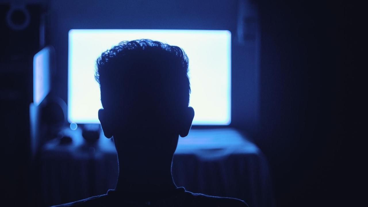 Ein Mann sitzt in einem dunklen Raum vor einem hell erleuchtenden Monitor. Ein Mann sitzt in einem dunklen Raum vor einem hell erleuchtenden Monitor.