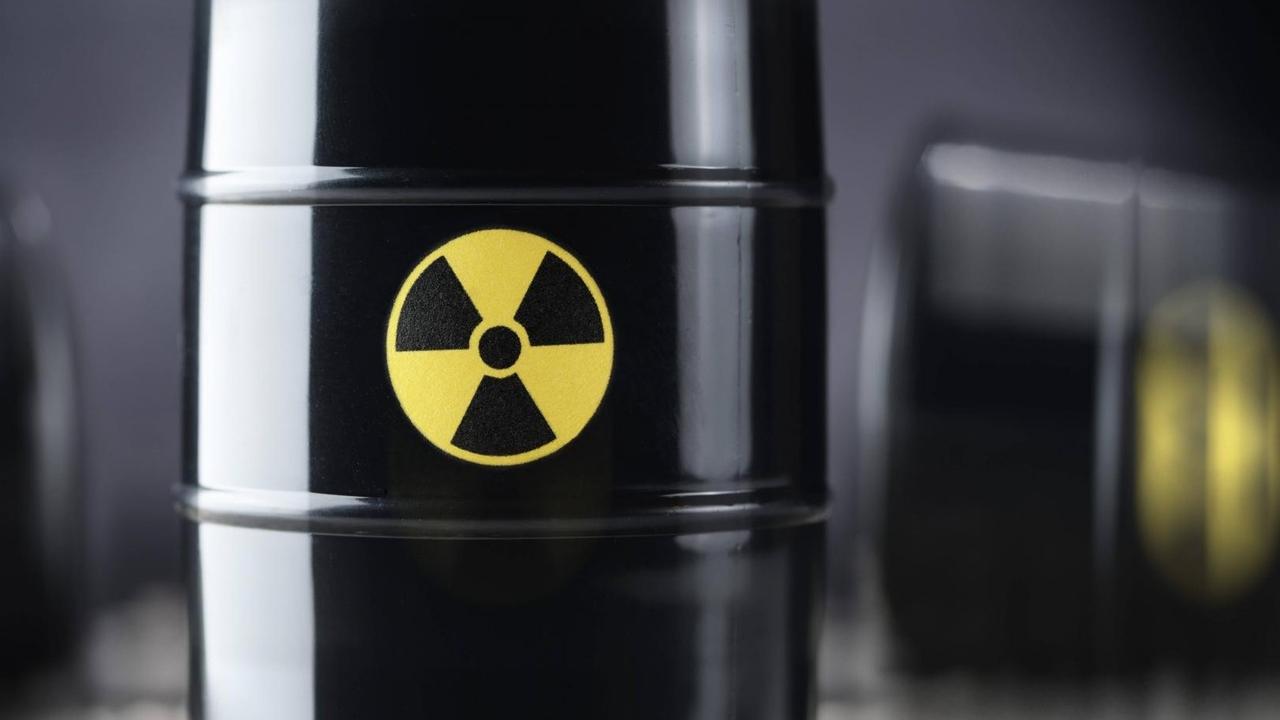 Drei schwarze Atommüll-Fässer, wobei eines im Vordergrund in der Mitte scharf abgebildet ist, im Hintergrund zwei weitere Fässer unscharf. Drei schwarze Atommüll-Fässer, wobei eines im Vordergrund in der Mitte scharf abgebildet ist, im Hintergrund zwei weitere Fässer unscharf.