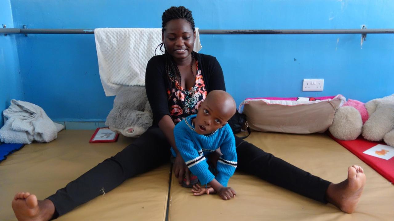 Zentrum für behinderte Kinder im kenianischen Mukuru. Auch der kleine Jeremy hat Hirnschäden infolge Sauerstoffmangels durch zu lange Wehen erlitten. Er sitzt auf dem Bett mit Betreuerin. Zentrum für behinderte Kinder im kenianischen Mukuru. Auch der kleine Jeremy hat Hirnschäden infolge Sauerstoffmangels durch zu lange Wehen erlitten. Er sitzt auf dem Bett mit Betreuerin.