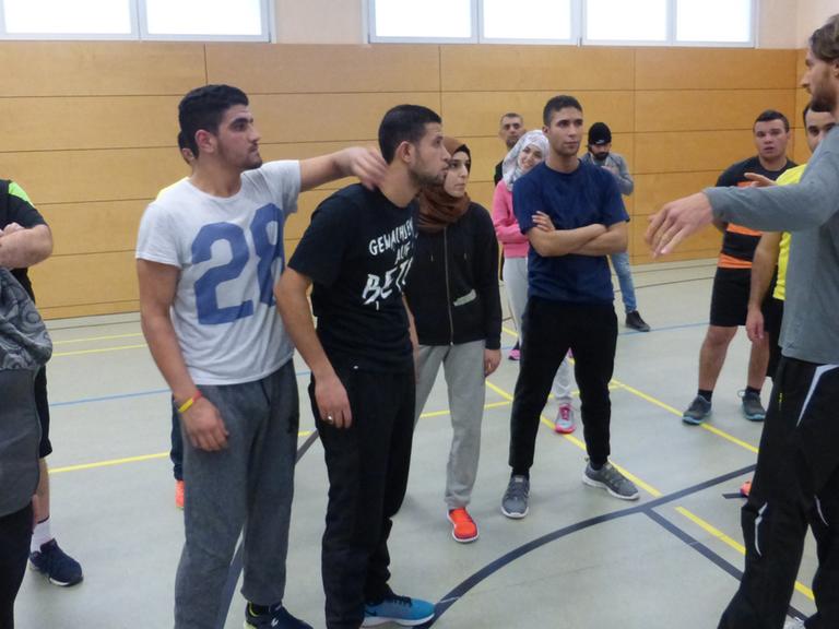 Flüchtlinge stehen in einer Berliner Sporthalle und hören einem Trainer zu.