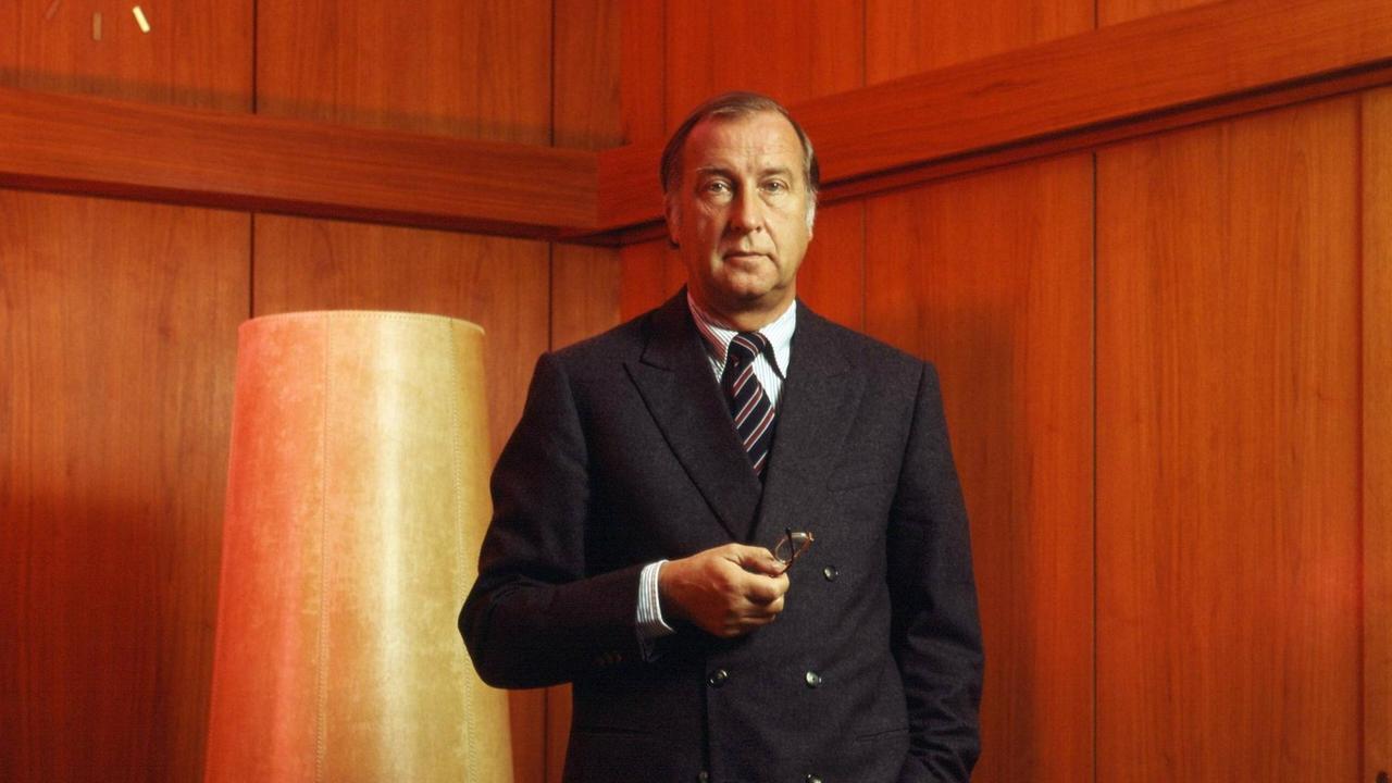 Ein noch analog fotografiertes Farbporträt des Treuhand-Präsidenten Detlef Rohwedder in Anzug und Krawatte und selbstbewußter Pose mit nachdenklicher Mimik vor einer Holz vertäfelten Wand.