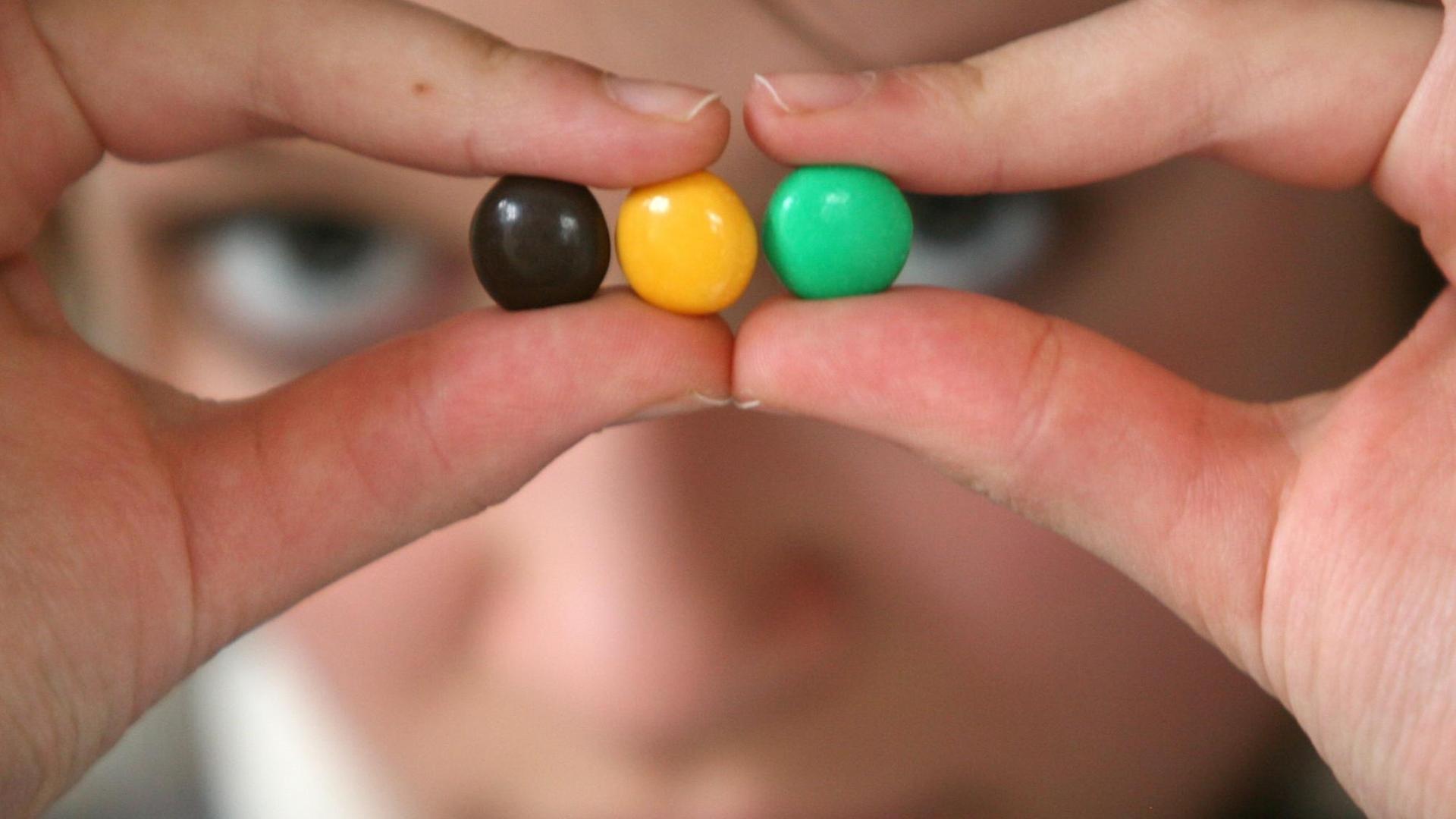 Symbolbild - Ein junges Mädchen hält schwarze, gelbe und grüne "Smarties" als Symbol für eine Jamaika-Koalition in der Hand. Symbolbild - Ein junges Mädchen hält schwarze, gelbe und grüne "Smarties" als Symbol für eine Jamaika-Koalition in der Hand.