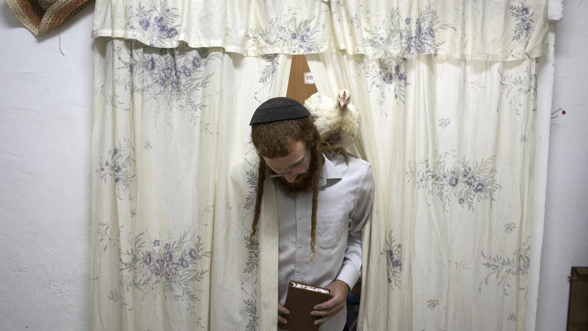 Ein jüdischer Mann mit Kippa und einem Huhn auf der Schulter betritt das Zimmer durch einen geblümten Vorhang.