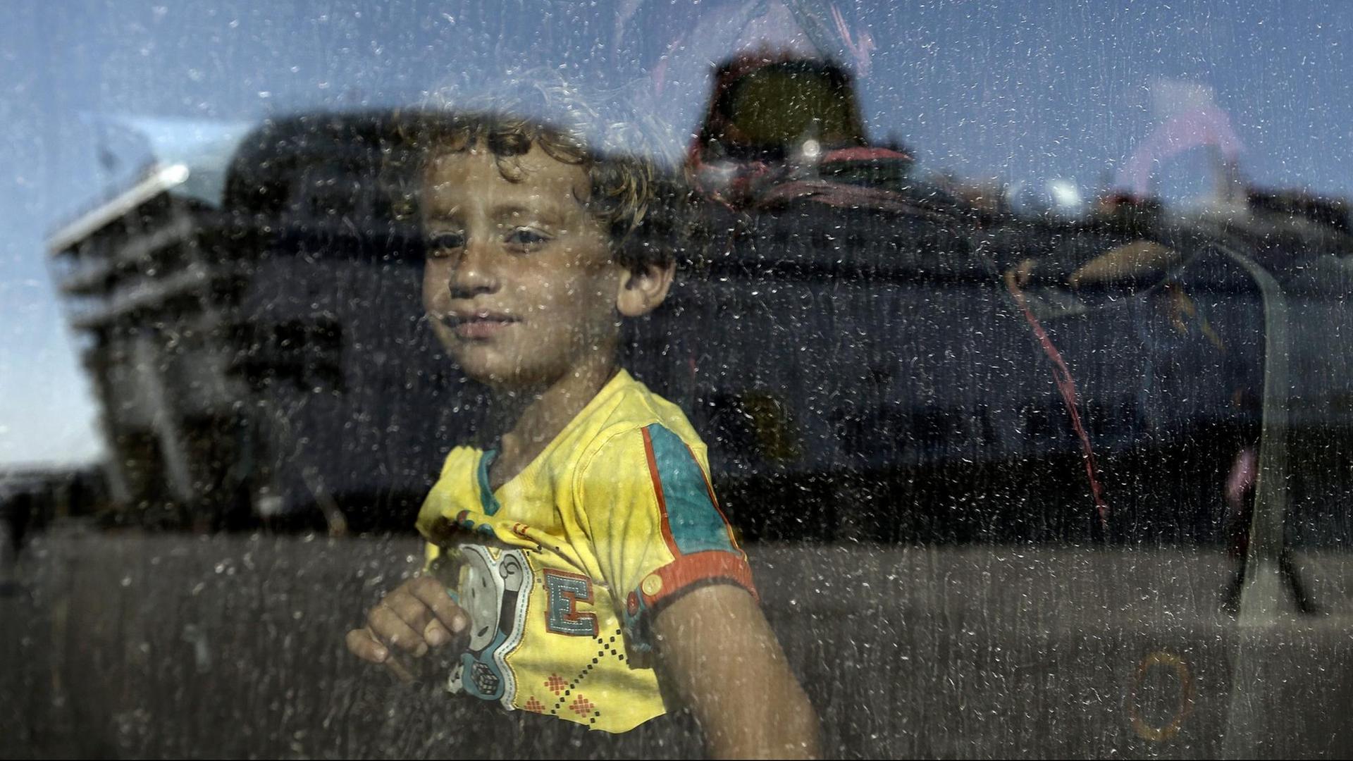 Ein Kind aus Syrien schaut in einen Bus, als gerade die Fähre 'Eleftherios Venizelos' in dessen Scheibe gespiegelt wird. Ein Kind aus Syrien schaut in einen Bus, als gerade die Fähre 'Eleftherios Venizelos' in dessen Scheibe gespiegelt wird.