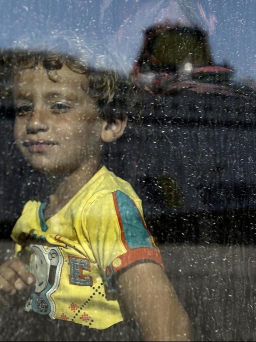 epaselect epa04897853: Ein Kind aus Syrien schaut in einen Bus, als gerade die Fähre 'Eleftherios Venizelos' in dessen Scheibe gespiegelt wird, nachdem sie im Hafen von Piräus nahe Athen/Griechenland am 25. August 2015 angekommen ist. EPA/YANNIS KOLESIDIS