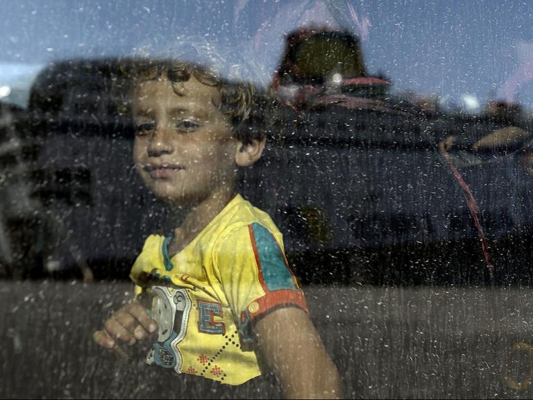 epaselect epa04897853: Ein Kind aus Syrien schaut in einen Bus, als gerade die Fähre 'Eleftherios Venizelos' in dessen Scheibe gespiegelt wird, nachdem sie im Hafen von Piräus nahe Athen/Griechenland am 25. August 2015 angekommen ist. EPA/YANNIS KOLESIDIS