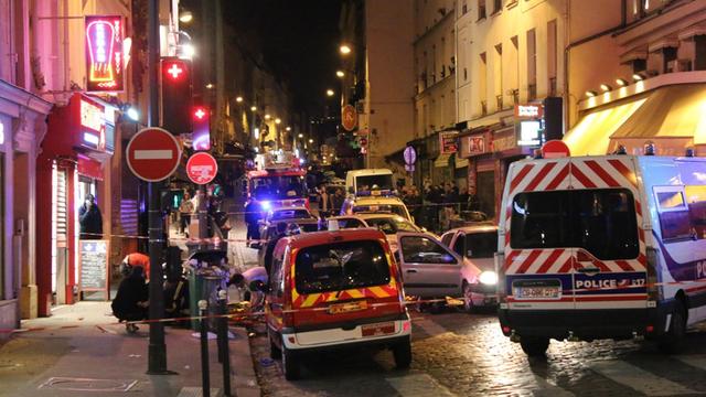 Straßenszene, Paris bei Nacht: Polizeifahrzeuge blockieren eine Straße, dahinter stauen sich Autos.