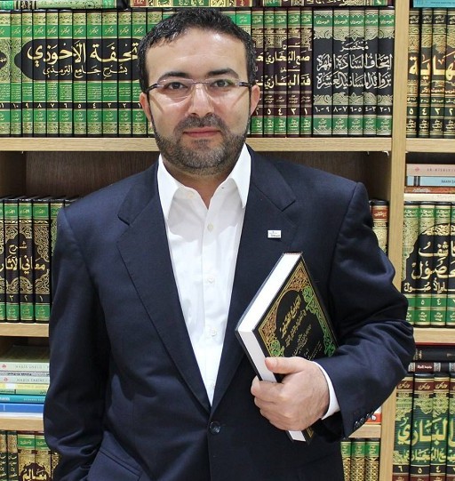 Professor Hüseyin İlker Çınar mit einem Buch in der Hand vor einem Bücherregal mit arabischen Büchern.