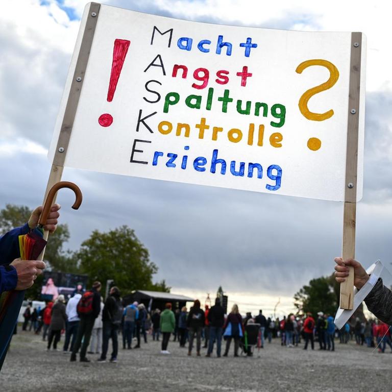 Zwei Menschen halten am Rande des Gottesdienstes der Querdenker ein Transparent in die Höhe, auf dem steht: "Macht, Angst, Spaltung, Kontrolle, Erziehung?"