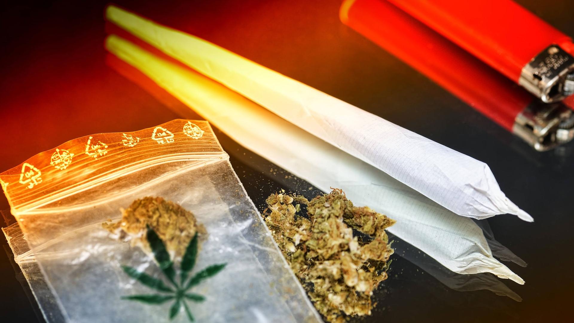 Auf einem Tisch liegt ein Plastiktütchen mit Hanf neben einem Joint und einem roten Feuerzeug. Auf einem Tisch liegt ein Plastiktütchen mit Hanf neben einem Joint und einem roten Feuerzeug.
