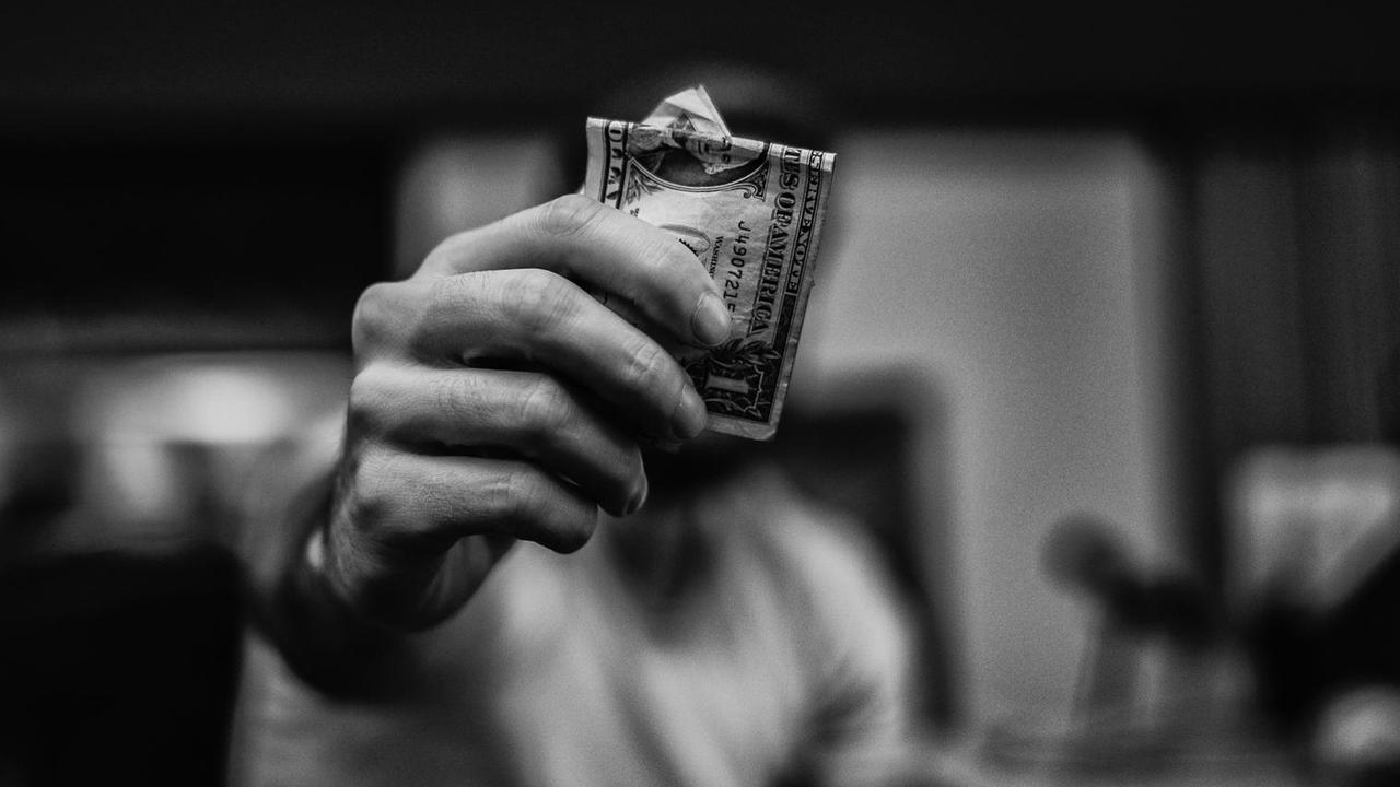 Eine Hand hält einen Dollarschein in die Kamera, der Kopf versteckt sich dahinter. Eine Hand hält einen Dollarschein in die Kamera, der Kopf versteckt sich dahinter.