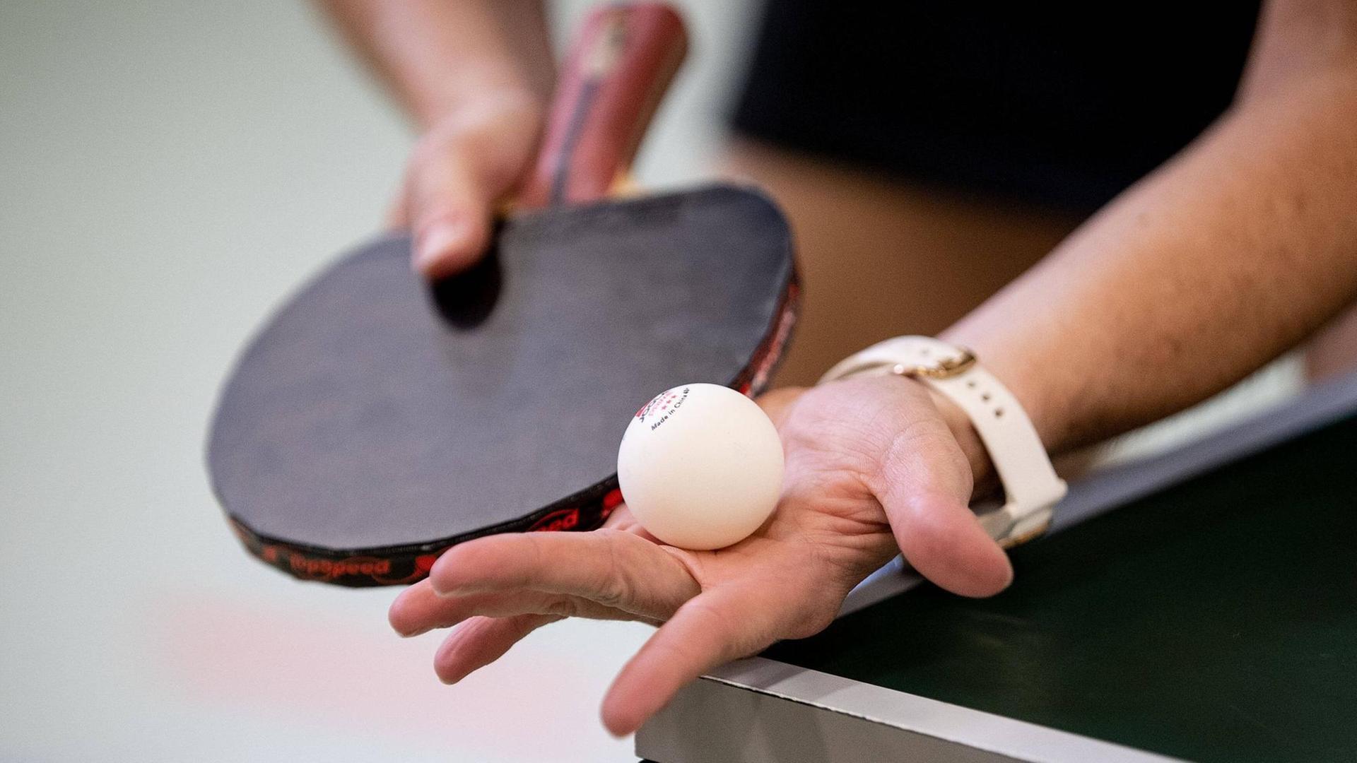 Eine Hand hät einen Tischtennisball direkt vor dem Aufschlag, die andere den Schläger Eine Hand hät einen Tischtennisball direkt vor dem Aufschlag, die andere den Schläger