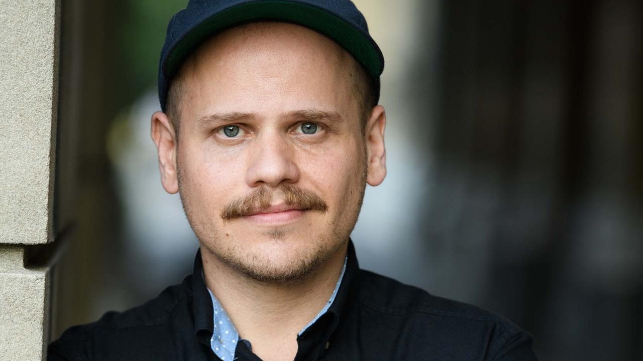 Ein junger Mann mit Basecap steht angelehnt an einer Wand. Ein junger Mann mit Basecap steht angelehnt an einer Wand.