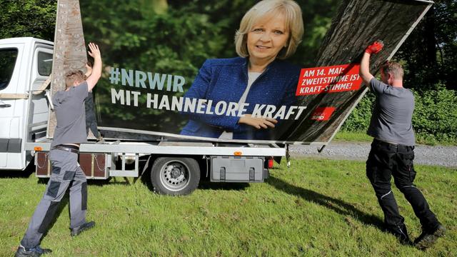 Zwei Arbeiter heben ein großes Wahlplakat von Hannelore Kraft (SPD) auf einen Laster.