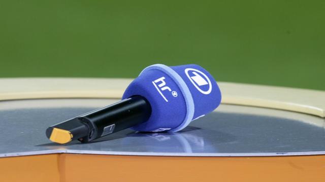 Auf einem Tisch liegt ein Mikrofon, auf dem das Logo des Hessischen Rundfunks prangt.