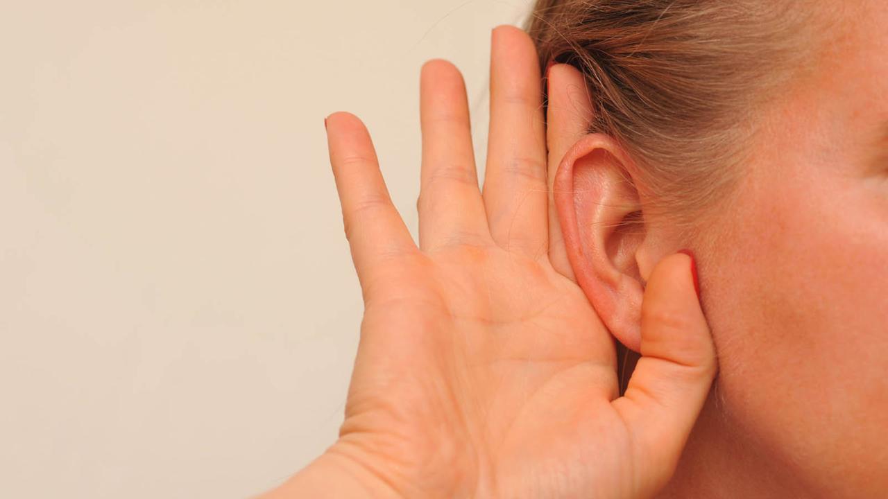 Eine Frau hält sich eine Hand ans Ohr. Eine Frau hält sich eine Hand ans Ohr.