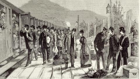 Gravurbild des Bahnhofs im italienischen Ventimiglia 1884. Reisende stehen neben einem Zug.