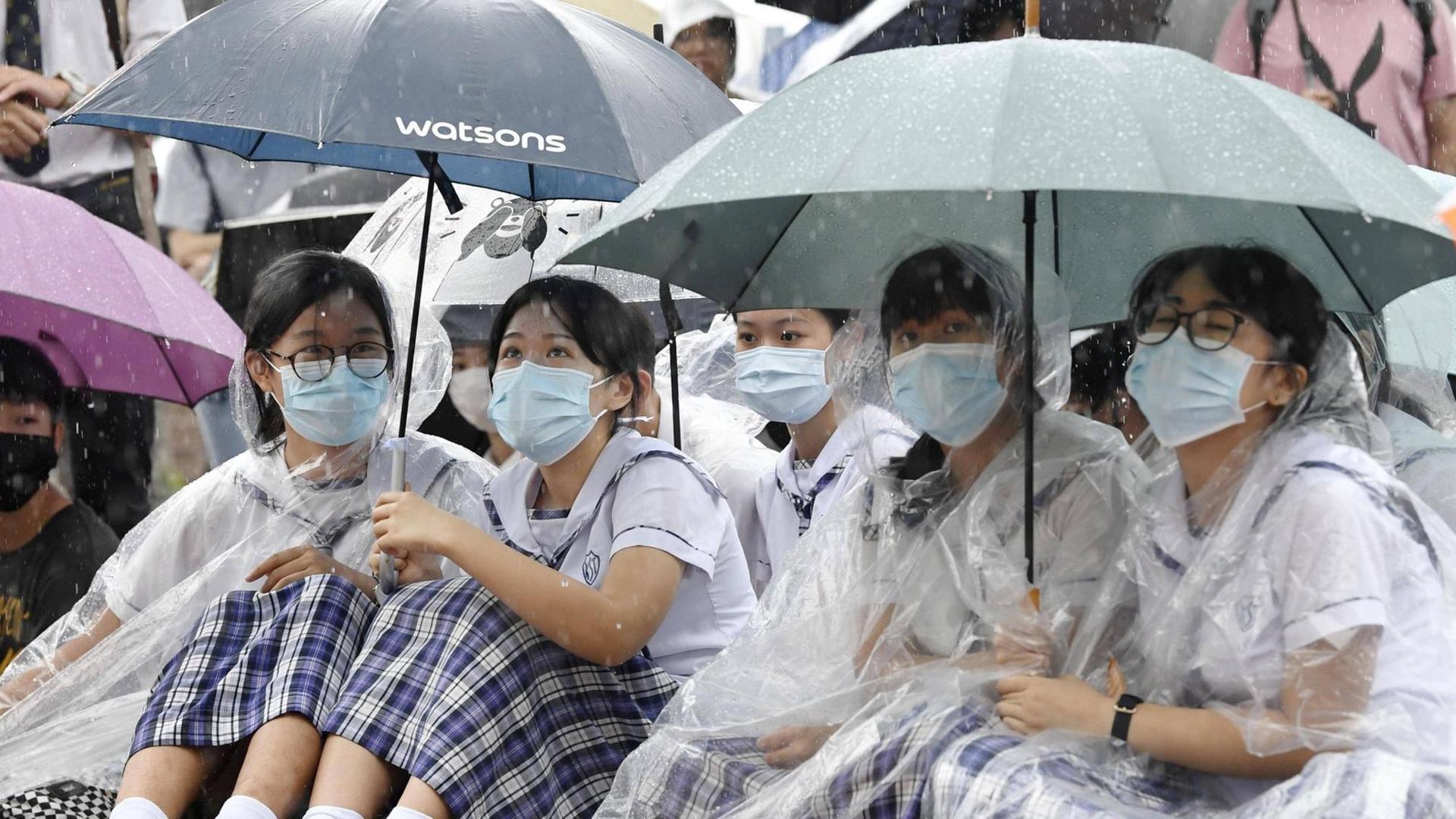 Mit Regenschirmen, Regenumhängen und Munschutz sitzen chinesische Studentinnen bei den Hongkonger Protesten auf der Straße. Mit Regenschirmen, Regenumhängen und Munschutz sitzen chinesische Studentinnen bei den Hongkonger Protesten auf der Straße.