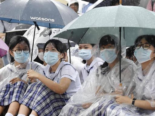 Mit Regenschirmen, Regenumhängen und Munschutz sitzen chinesische Studentinnen bei den Hongkonger Protesten auf der Straße.