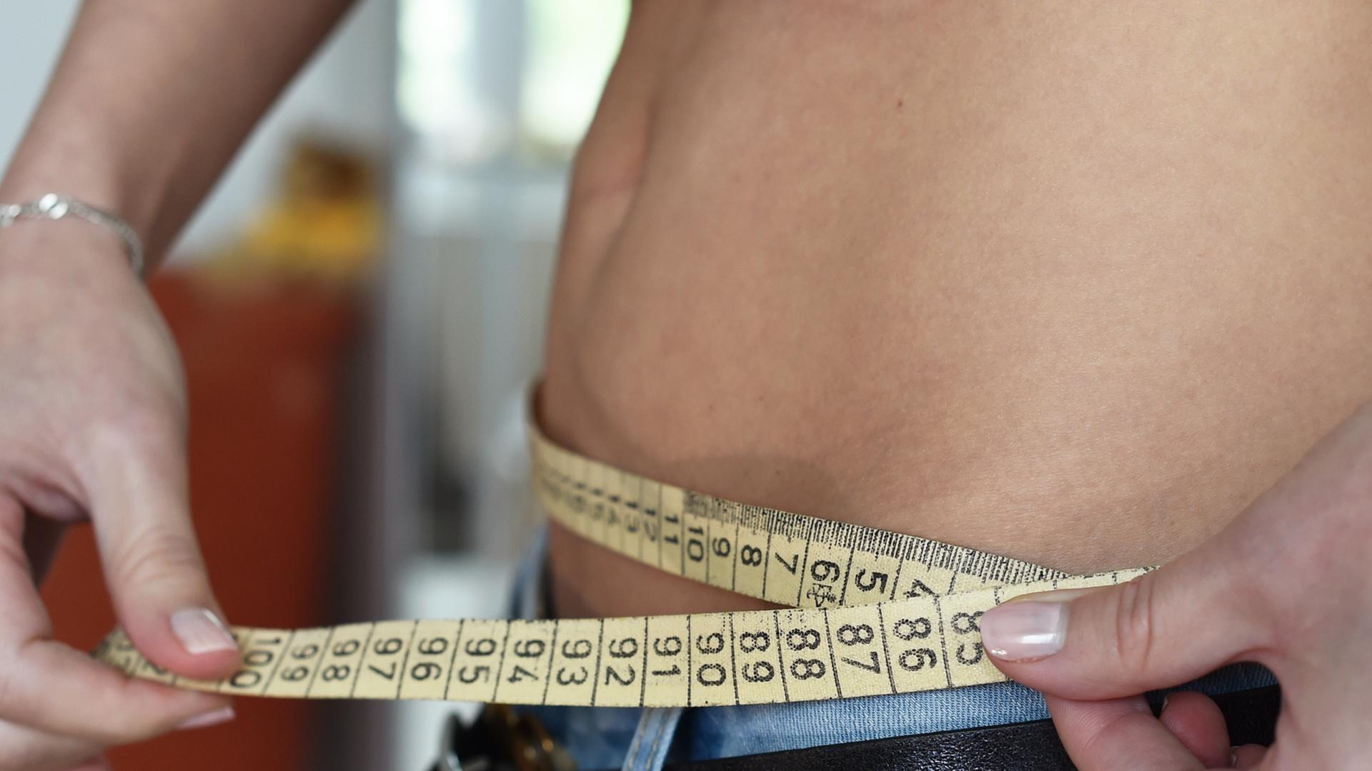 Ein Zentimetermaß ist um den Bauch einer Frau gewunden. Ein Zentimetermaß ist um den Bauch einer Frau gewunden.