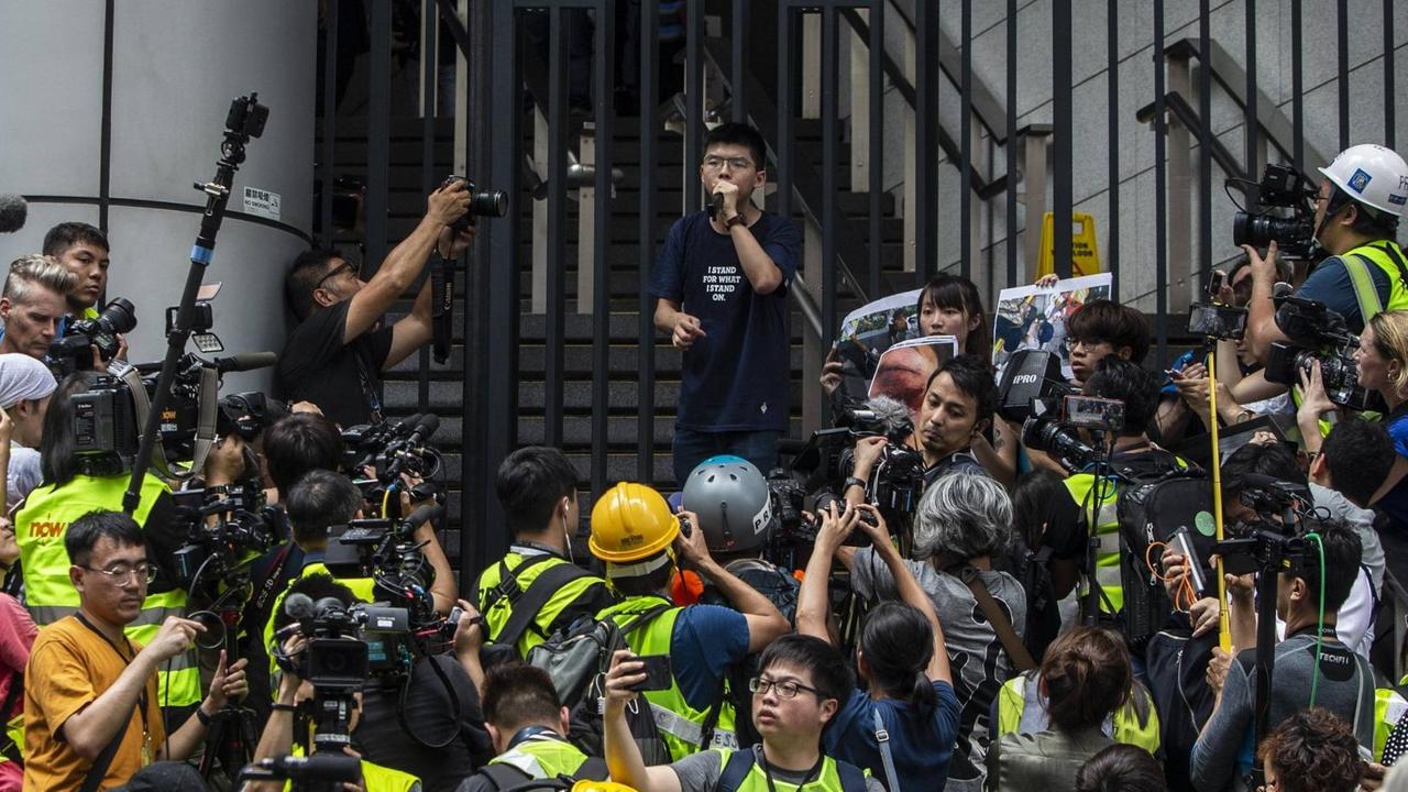 Joshua Wong steht vor den Toren des Hongkonger Polizeipräsidiums. Umringt von Journalisten und Kameras spricht er zu Demonstranten. Joshua Wong steht vor den Toren des Hongkonger Polizeipräsidiums. Umringt von Journalisten und Kameras spricht er zu Demonstranten.